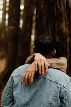 a man and woman hugging in the woods with their hands on each other's shoulders