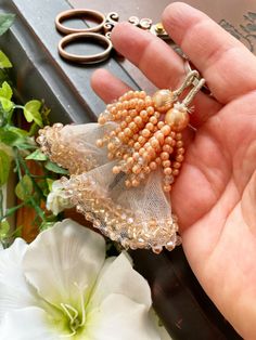 a person holding some beads in their hand next to flowers and an open pair of scissors