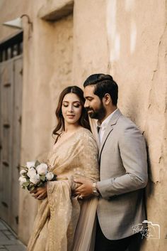 a man and woman standing next to each other in front of a wall with flowers