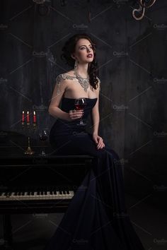 a woman sitting at a piano with a glass of wine in her hand and candles on the table behind her