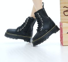 a close up of a person's legs wearing black boots and standing next to a wooden block