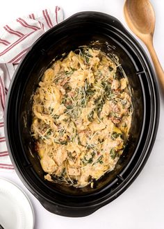 a crock pot filled with pasta and spinach on top of a white table