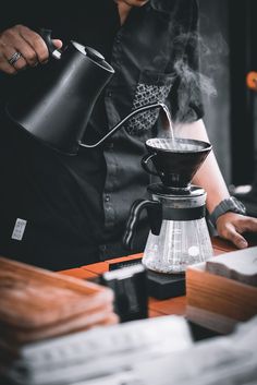 a man pours coffee into a glass cup on top of a wooden table with other items