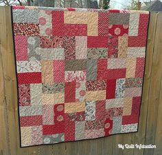 a red and gray quilt hanging on a fence next to a wooden fence with a tree in the background