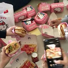 several people holding sandwiches and cell phones at a table with hello kitty boxes on it