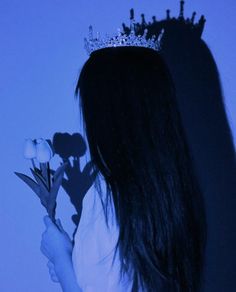 a woman wearing a tiara and holding a flower in her hand with the shadow of a crown on her head