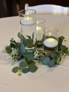 three candles are sitting on a table with greenery