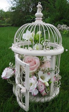 a white birdcage filled with flowers on top of green grass in a field