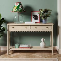 a white table with two drawers and a lamp on it next to a potted plant