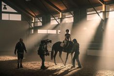 a woman riding on the back of a horse in an indoor arena with people standing around