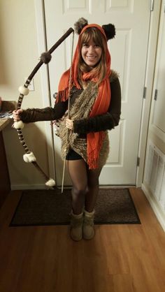 a woman dressed up as a racoon holding a stick and wearing an orange scarf