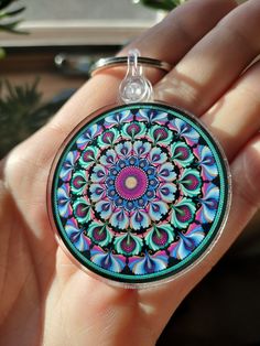 a hand holding a colorful glass pendant with a circular design on it's side