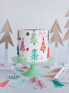 a decorated christmas cake sitting on top of a table next to cut paper tree decorations