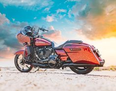 a red motorcycle parked on top of a sandy beach under a cloudy blue and yellow sky