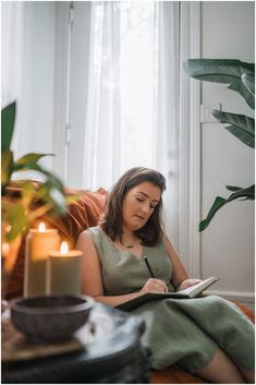 a woman sitting on a couch with a book in her hand and candles around her