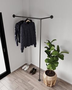 a clothes rack with two sweaters hanging on it next to a potted plant