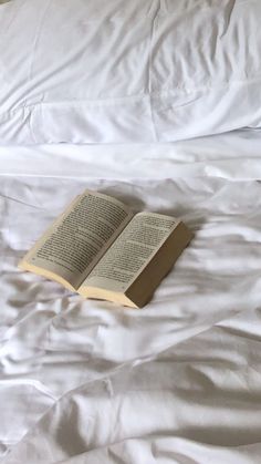 an open book laying on top of a white bed