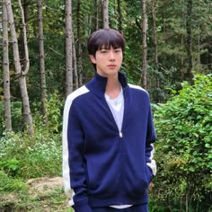 a young man standing in front of trees wearing a blue jacket and white t - shirt