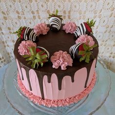 a heart shaped chocolate cake with pink flowers and strawberries on top, sitting on a glass platter