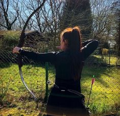 a woman holding a bow and arrow while standing in front of a fenced area