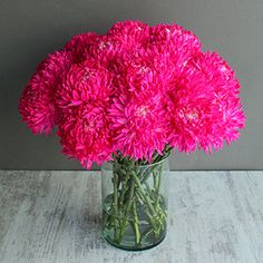 a vase filled with pink flowers sitting on top of a wooden table next to a gray wall