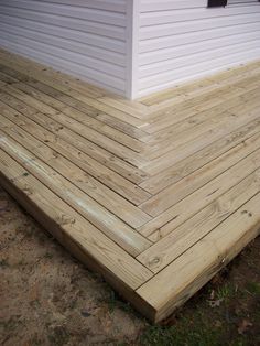 a wooden deck in front of a house with white siding on the side of it