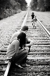 three people sitting on train tracks with one person looking at the camera