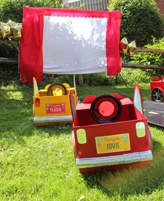 some toys are sitting in the grass near a red and yellow truck with a white banner