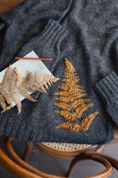 a sweater with fern leaves on it sitting on top of a wooden table next to a pair of scissors