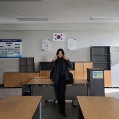 a woman standing in front of desks talking on her cell phone while wearing a blazer