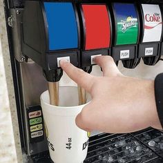 a person's hand is pressing the button on a coffee machine with four cups in it