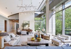 a living room filled with lots of furniture and large windows overlooking the trees in the background