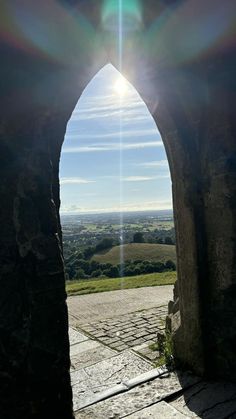 the sun is shining through an arch in a stone wall with a view of countryside below