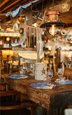 a wooden table topped with blue plates and wine glasses next to a lamp hanging from the ceiling