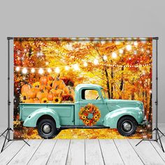 an old blue truck with pumpkins on the back in front of a fall scene