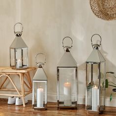 three metal lanterns sitting on top of a wooden floor next to a table with candles