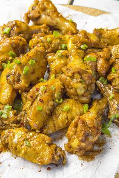 chicken wings covered in sauce and green onions on a piece of parchment paper with seasoning sprinkled around the edges