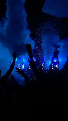 people are in the dark with their hands up and fireworks coming from behind them at a concert