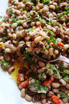 a white plate topped with black - eyed beans and greens next to a spoon filled with dressing