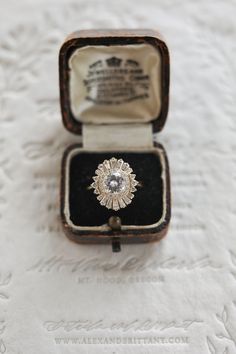 an antique diamond ring sits in its box on a white tableclothed cloth covered surface