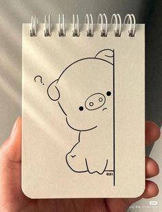 a hand holding a notebook with a drawing of a pig on it