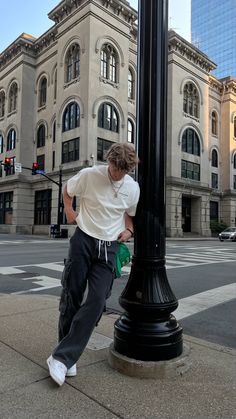 A streetwear outfit for the spring and summer. The outfit is simple and easy to replicate. The top is a cream, boxy-fit t-shirt and the pants are wide leg cargo pants in washed black denim. The accessories are a white shoe string belt, a Kelly green trucker hat, and all white Jordan 4 sneakers. Summer Male Streetwear, Casual Western Men Outfit, Guys Streetwear Aesthetic, Trendy Outfits Guys, Guy Poses Aesthetic, Men Streetwear Accessories, Guy Summer Outfits Casual Street Styles, Men Graphic Tee Outfit Mens Fashion, Men’s Baggy Style