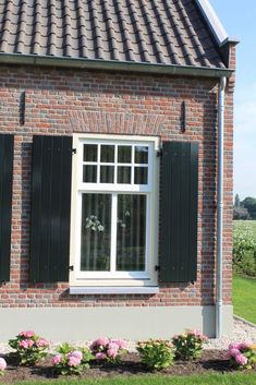 a brick house with green shutters and pink flowers