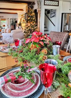 the table is set for christmas dinner with red dishes and silverware, greenery and candlesticks