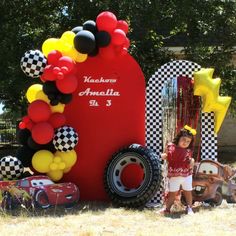 a young boy standing next to a giant red truck with balloons on it's side