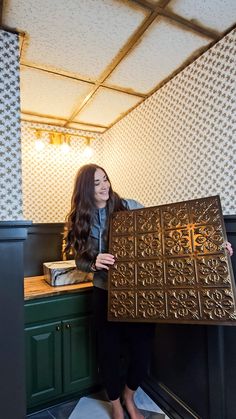 a woman standing in front of a counter holding up a large piece of metal tile