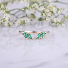 two gold rings with green stones on them sitting next to white flowers and greenery