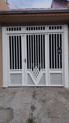 a white gate that is on the side of a building with an open door in front of it