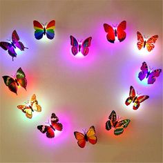 many colorful butterflies are arranged in the shape of a heart on a white surface with pink and blue lights