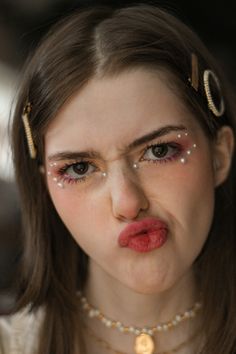 a woman with makeup on her face making a funny face while wearing pearls and gold jewelry